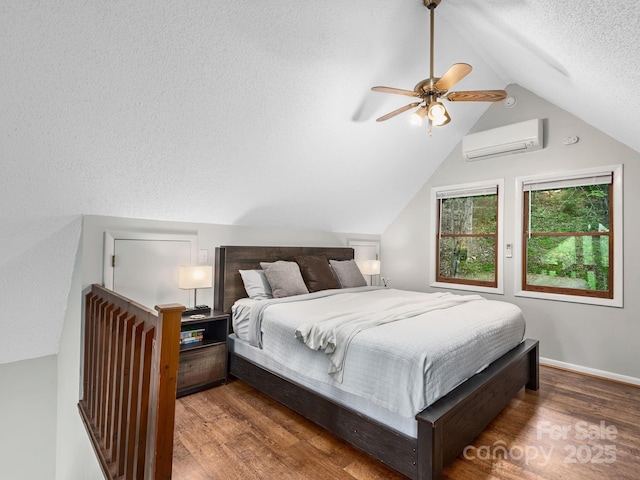 bedroom with an AC wall unit, a textured ceiling, baseboards, wood finished floors, and vaulted ceiling