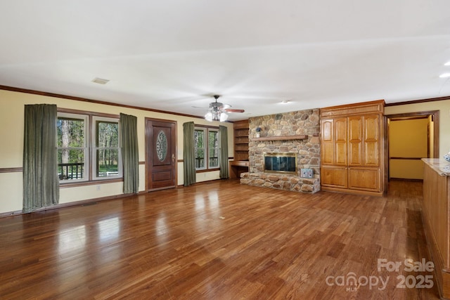 unfurnished living room featuring visible vents, ceiling fan, a stone fireplace, crown molding, and wood finished floors