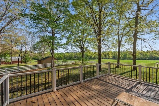 deck featuring a rural view, fence, an outdoor structure, and a lawn