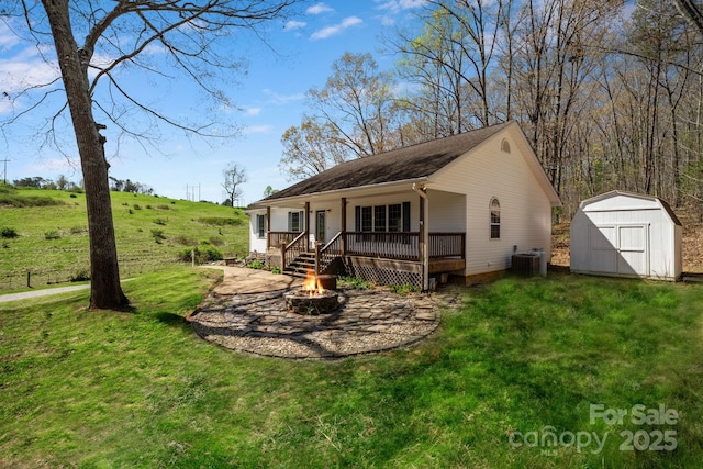 rear view of property featuring a fire pit, central AC, an outbuilding, a lawn, and a storage unit