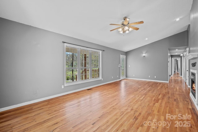 unfurnished living room with visible vents, ceiling fan, light wood-style floors, a lit fireplace, and lofted ceiling
