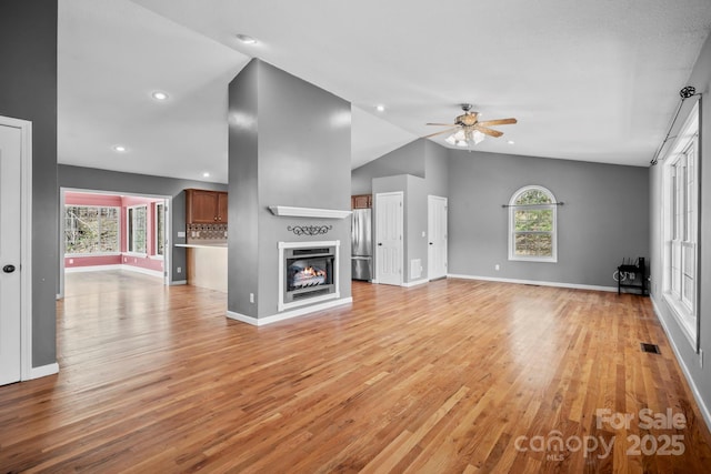 unfurnished living room featuring a healthy amount of sunlight, lofted ceiling, a ceiling fan, and visible vents