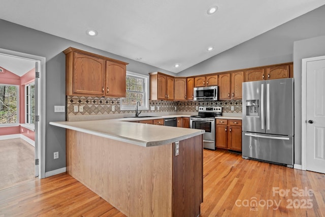 kitchen with brown cabinetry, appliances with stainless steel finishes, a sink, and lofted ceiling