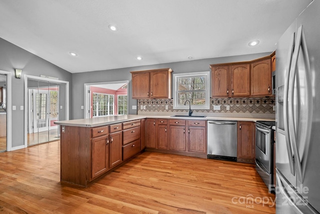 kitchen with light wood-style floors, a peninsula, light countertops, a sink, and stainless steel appliances