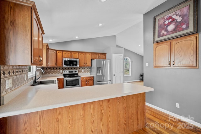 kitchen featuring a sink, light countertops, appliances with stainless steel finishes, a peninsula, and lofted ceiling