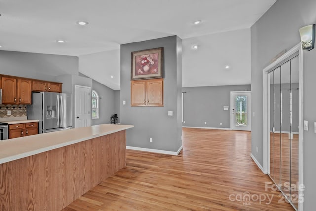 kitchen with baseboards, light wood-style flooring, light countertops, decorative backsplash, and appliances with stainless steel finishes