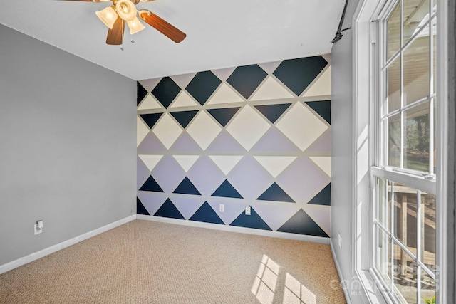 unfurnished room featuring an accent wall, ceiling fan, baseboards, and carpet