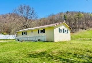 rear view of property featuring a forest view, fence, and a lawn