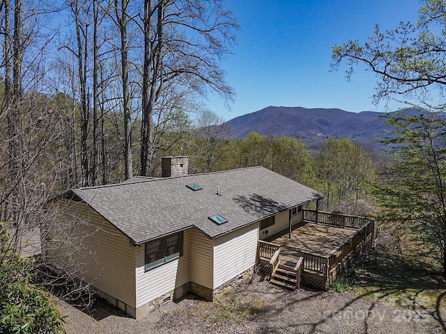 exterior space with a deck with mountain view, a shingled roof, and a chimney