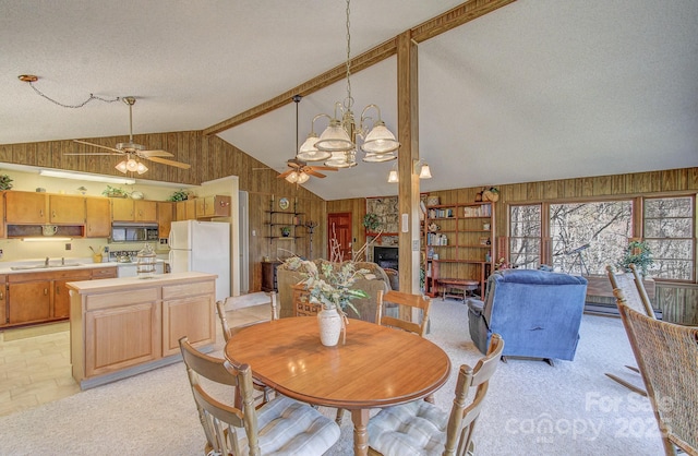 dining space featuring wood walls, lofted ceiling with beams, and ceiling fan with notable chandelier