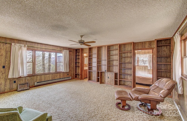 sitting room featuring wood walls, a baseboard radiator, a ceiling fan, and carpet flooring