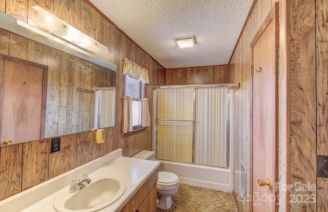 full bathroom with toilet, a textured ceiling, wooden walls, vanity, and shower / bath combination with glass door
