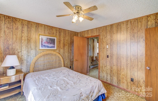 bedroom featuring baseboard heating, a textured ceiling, wooden walls, and a ceiling fan