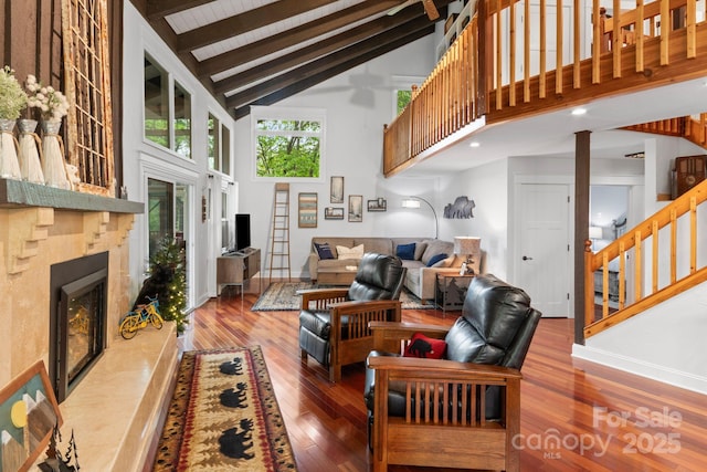 living room featuring hardwood / wood-style floors, beamed ceiling, baseboards, high vaulted ceiling, and a fireplace with raised hearth