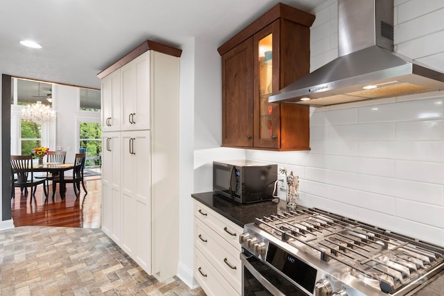 kitchen featuring wall chimney range hood, gas range, black microwave, glass insert cabinets, and brick floor