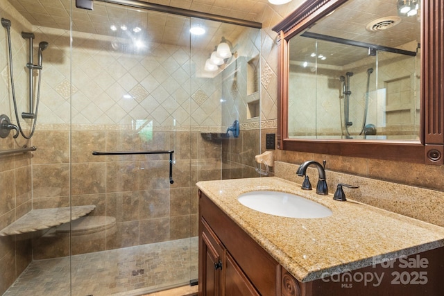 full bath featuring vanity, a stall shower, visible vents, and tile walls