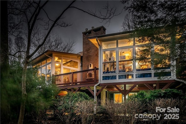 back of house at twilight with a sunroom and a chimney