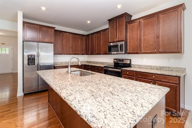 kitchen with a kitchen island with sink, a sink, baseboards, light wood-style floors, and stainless steel appliances
