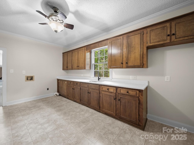 kitchen featuring ceiling fan, ornamental molding, light countertops, a sink, and baseboards