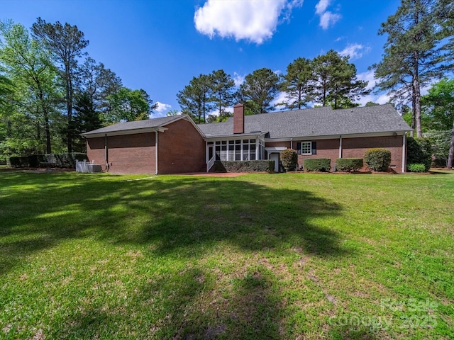 back of property with brick siding, central air condition unit, a lawn, and a chimney
