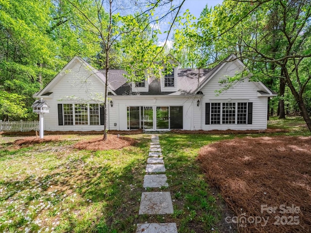 back of house featuring a shingled roof, fence, and a lawn