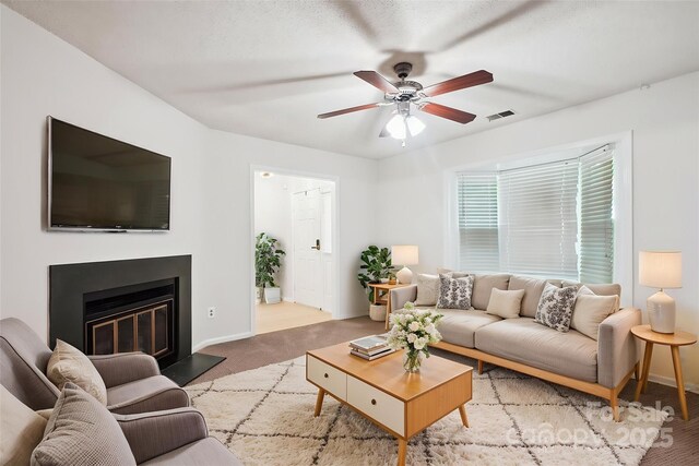 living area with a ceiling fan, visible vents, baseboards, carpet floors, and a glass covered fireplace