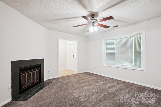 unfurnished living room featuring a ceiling fan, a textured ceiling, visible vents, a fireplace with flush hearth, and carpet flooring