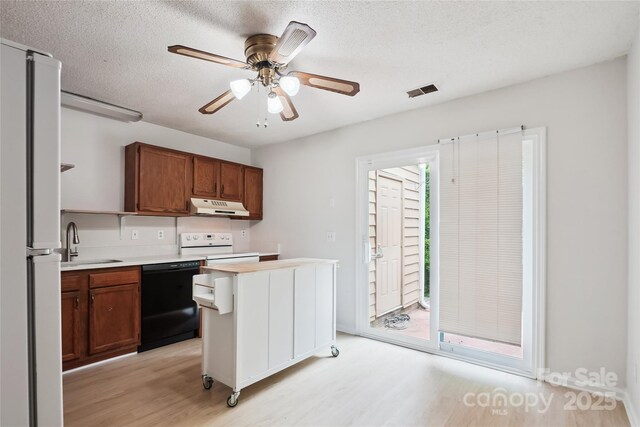 kitchen with a sink, light countertops, light wood finished floors, under cabinet range hood, and white appliances