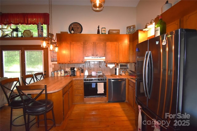 kitchen featuring stainless steel dishwasher, freestanding refrigerator, a peninsula, stove, and under cabinet range hood