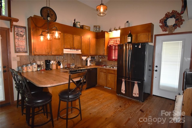 kitchen featuring under cabinet range hood, a peninsula, black appliances, and light wood-style floors