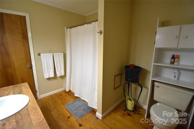 full bathroom featuring crown molding, wood finished floors, toilet, baseboards, and a sink