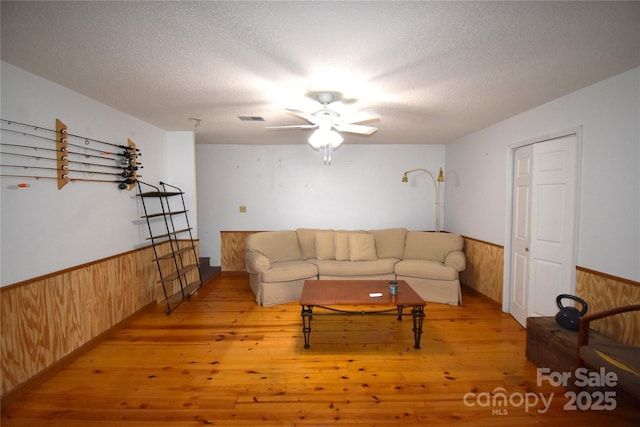living area with visible vents, wood walls, wainscoting, ceiling fan, and light wood-type flooring