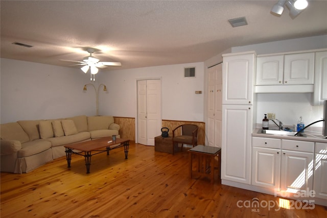 living room featuring visible vents, light wood-style flooring, ceiling fan, and a wainscoted wall