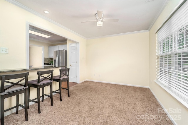 interior space featuring light carpet, baseboards, ornamental molding, and ceiling fan