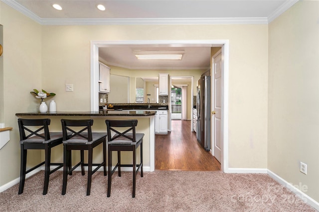 kitchen featuring a peninsula, carpet flooring, dark countertops, freestanding refrigerator, and white cabinetry