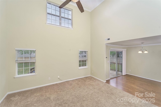 unfurnished living room with carpet flooring, plenty of natural light, baseboards, a towering ceiling, and crown molding