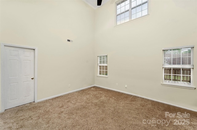 carpeted spare room featuring a high ceiling, baseboards, ceiling fan, and visible vents