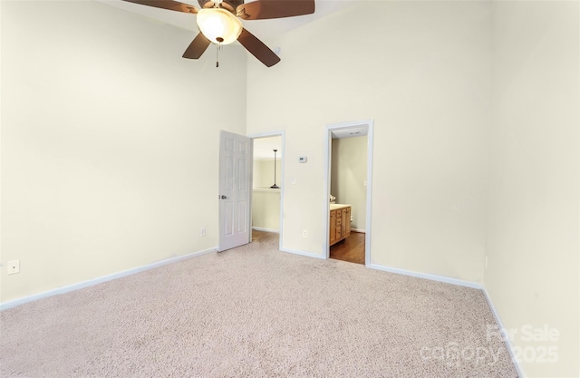 unfurnished bedroom featuring baseboards, carpet, a high ceiling, ensuite bath, and a walk in closet