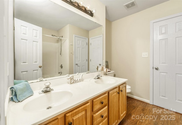 full bath featuring toilet, wood finished floors, a sink, and visible vents