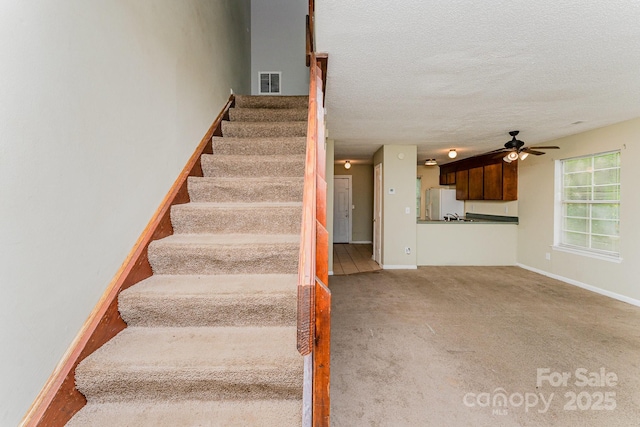 stairs featuring ceiling fan, carpet, a textured ceiling, visible vents, and baseboards