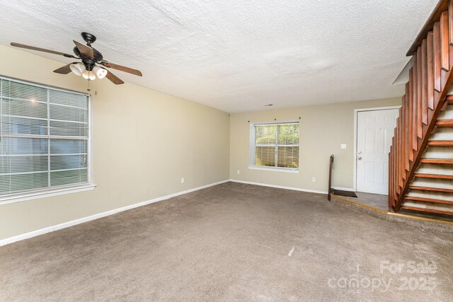 unfurnished living room featuring baseboards, a textured ceiling, a ceiling fan, stairs, and carpet
