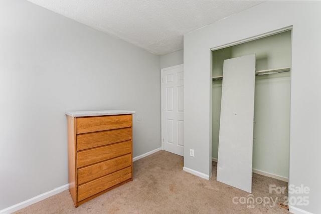 unfurnished bedroom with a textured ceiling, a closet, light colored carpet, and baseboards