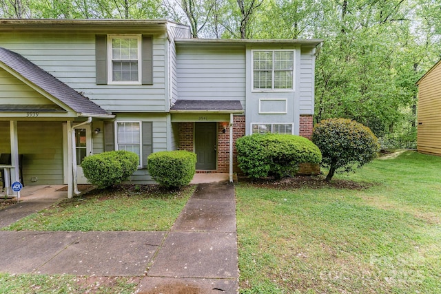 multi unit property with a shingled roof, brick siding, and a front lawn