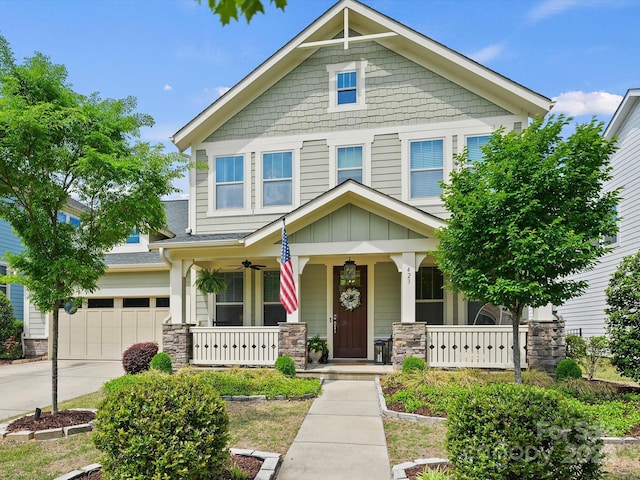 craftsman-style home with driveway, stone siding, covered porch, and a shingled roof