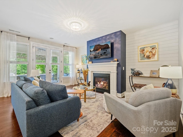 living area with wood finished floors, a glass covered fireplace, wooden walls, visible vents, and french doors