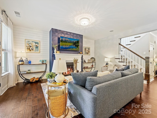 living room featuring visible vents, stairs, dark wood-type flooring, and a glass covered fireplace