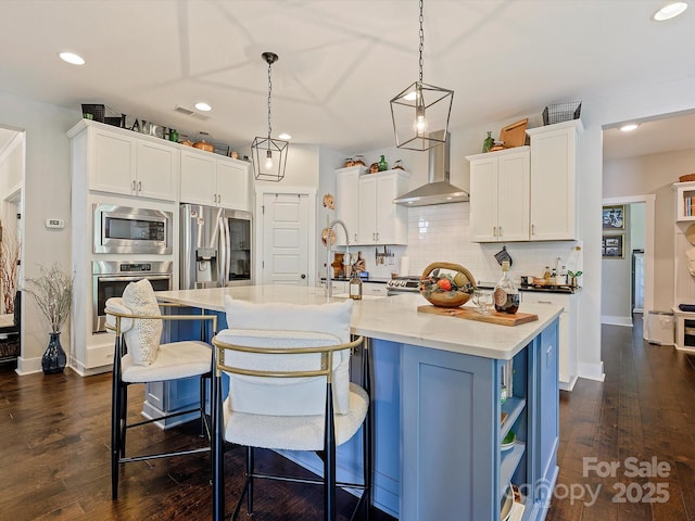 kitchen with wall chimney range hood, white cabinets, a sink, visible vents, and stainless steel appliances