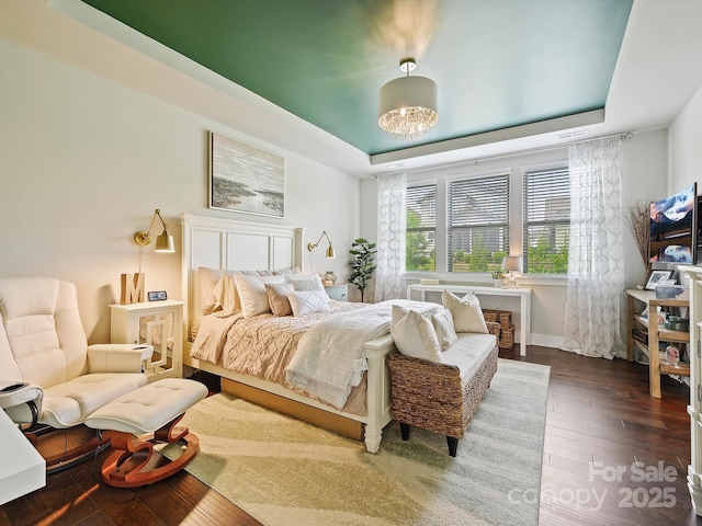 bedroom with baseboards, a raised ceiling, and hardwood / wood-style flooring