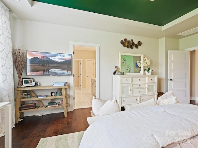 bedroom featuring hardwood / wood-style floors, ensuite bath, a raised ceiling, and visible vents