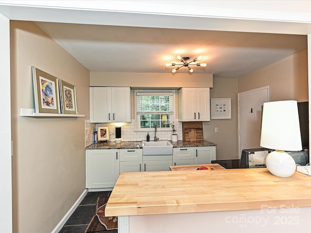 kitchen with baseboards, white cabinetry, wooden counters, decorative backsplash, and a sink